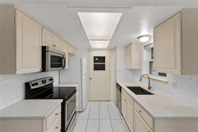 kitchen featuring stainless steel appliances, cream cabinetry, sink, and backsplash