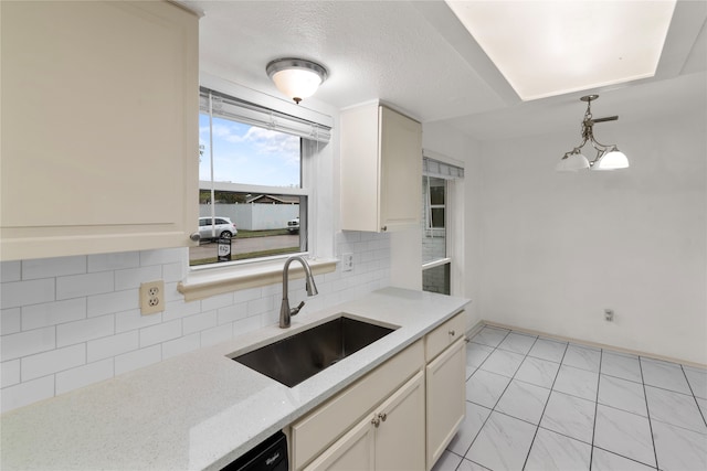 kitchen with sink, light stone counters, tasteful backsplash, a textured ceiling, and hanging light fixtures