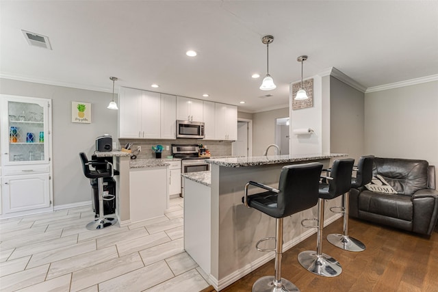 1401 Crescent Dr, Sherman, TX 75092 - kitchen featuring appliances with stainless steel finishes, ornamental molding, a kitchen bar, white cabinetry, and a peninsula