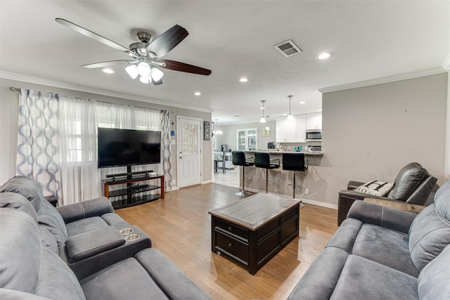 living room with recessed lighting, visible vents, light wood-style flooring, ornamental molding, and baseboards