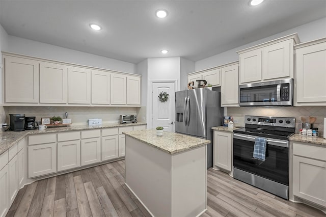 kitchen with appliances with stainless steel finishes, light stone counters, and light hardwood / wood-style flooring