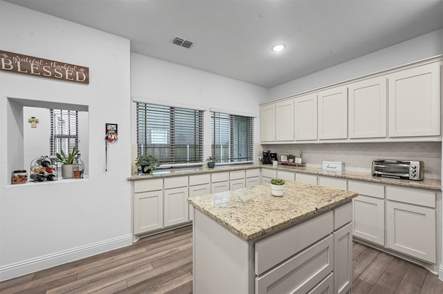 kitchen featuring white cabinets, light hardwood / wood-style floors, a kitchen island, and light stone countertops