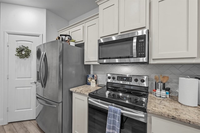 kitchen featuring light wood-type flooring, appliances with stainless steel finishes, light stone countertops, and white cabinets