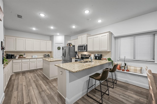 kitchen featuring wood-type flooring, a center island, white cabinets, a breakfast bar, and appliances with stainless steel finishes