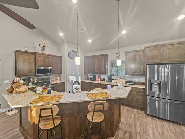 kitchen with appliances with stainless steel finishes, decorative light fixtures, a kitchen bar, and a kitchen island with sink