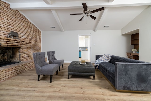 living room featuring lofted ceiling with beams, a fireplace, light wood-type flooring, ceiling fan, and brick wall