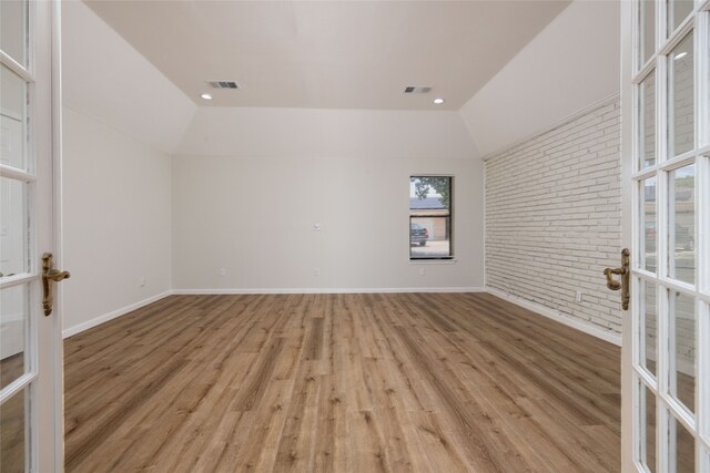 empty room featuring lofted ceiling, french doors, light hardwood / wood-style floors, and brick wall