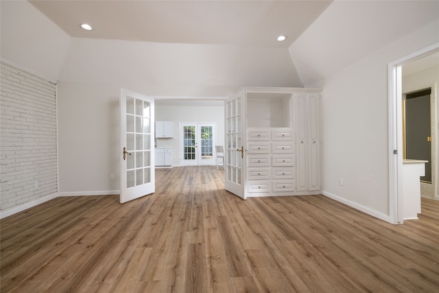 interior space featuring vaulted ceiling, brick wall, light hardwood / wood-style flooring, and french doors