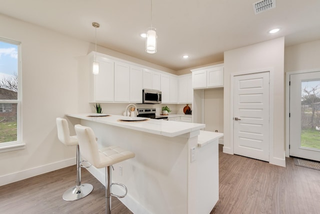 kitchen with stainless steel appliances, light countertops, visible vents, hanging light fixtures, and a peninsula