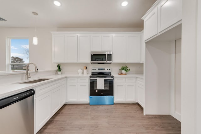 kitchen featuring decorative light fixtures, stainless steel appliances, light countertops, white cabinetry, and a sink