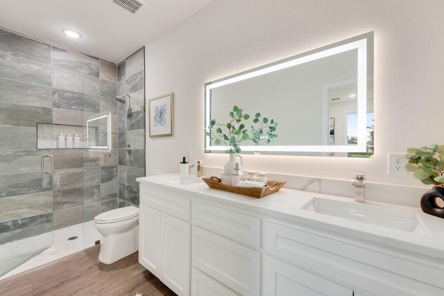 full bath with double vanity, toilet, wood finished floors, a shower stall, and a sink