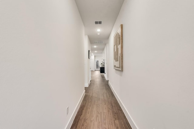 hall with visible vents, baseboards, and wood finished floors