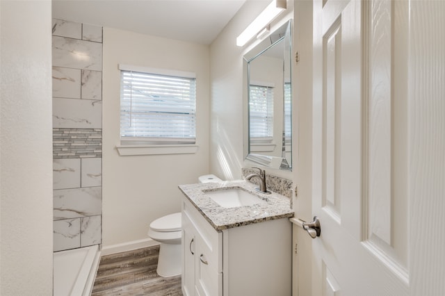 bathroom with a tile shower, hardwood / wood-style flooring, toilet, and vanity