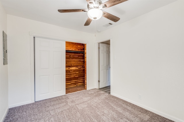 unfurnished bedroom with ceiling fan, electric panel, carpet floors, wooden walls, and a closet