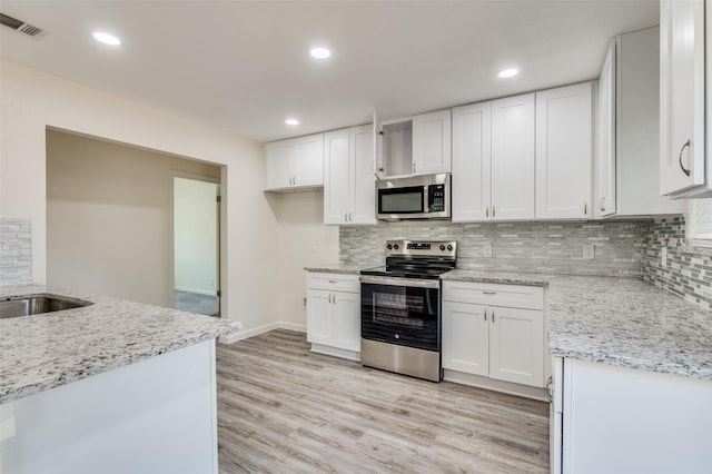 kitchen with light hardwood / wood-style flooring, appliances with stainless steel finishes, white cabinets, light stone counters, and decorative backsplash