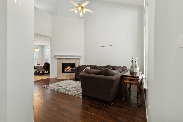 living room with dark hardwood / wood-style flooring, a high ceiling, a tiled fireplace, and ceiling fan