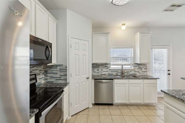 kitchen with dark stone countertops, white cabinetry, decorative backsplash, and stainless steel appliances