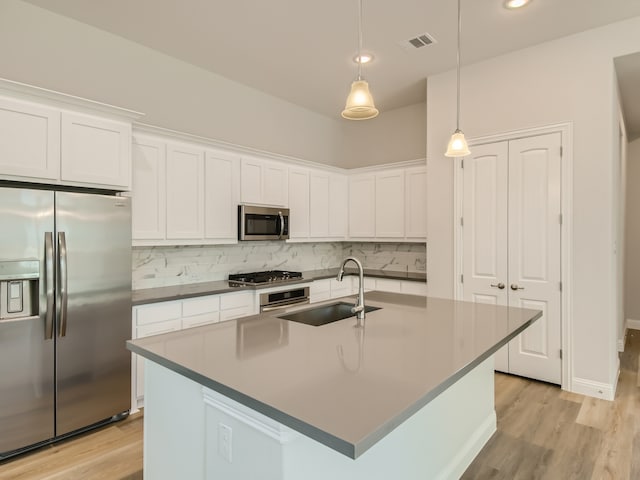 kitchen with stainless steel appliances, pendant lighting, sink, white cabinets, and a kitchen island with sink