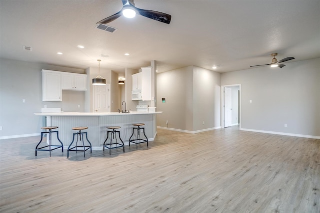 kitchen featuring light hardwood / wood-style floors, white cabinetry, a kitchen breakfast bar, ceiling fan, and decorative light fixtures