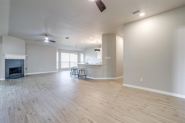 unfurnished living room with sink, a tile fireplace, ceiling fan, and light hardwood / wood-style flooring