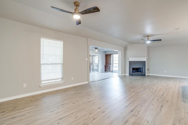 unfurnished living room with light hardwood / wood-style flooring, ceiling fan, vaulted ceiling, and a tile fireplace