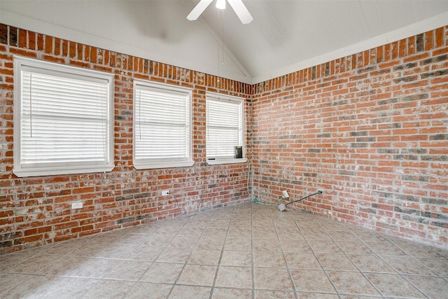 tiled empty room with a wealth of natural light, lofted ceiling, and brick wall