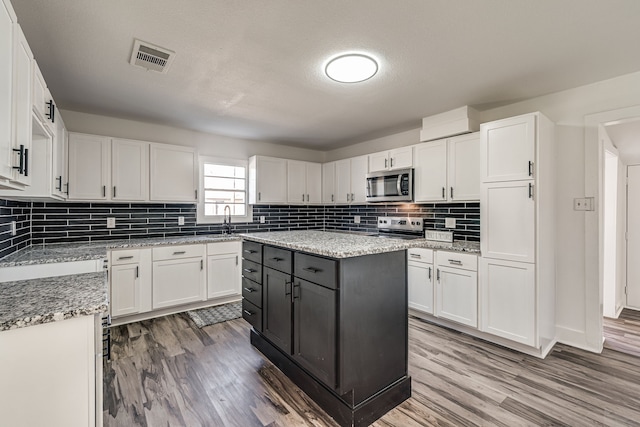 kitchen featuring white cabinetry, stainless steel appliances, wood-type flooring, and light stone counters