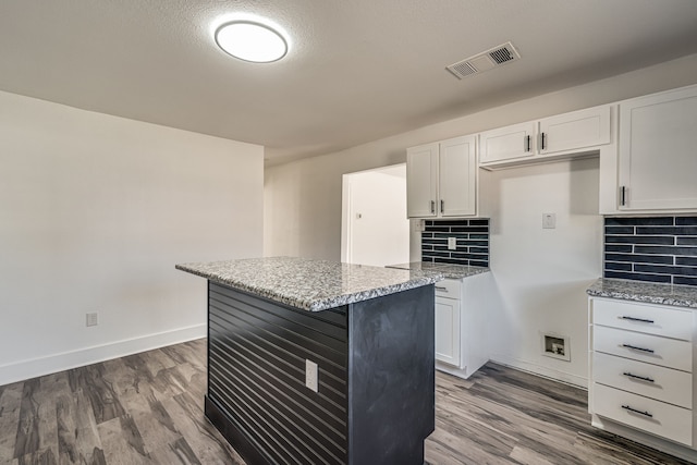 kitchen featuring light stone countertops, wood-type flooring, white cabinetry, and tasteful backsplash