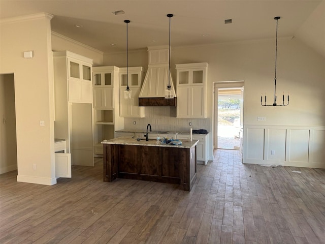 kitchen with wood-type flooring, an island with sink, decorative light fixtures, and custom range hood