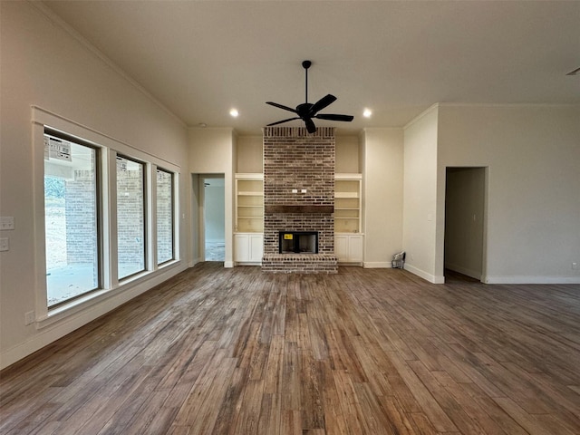 unfurnished living room featuring wood-type flooring, ceiling fan, ornamental molding, a fireplace, and built in shelves