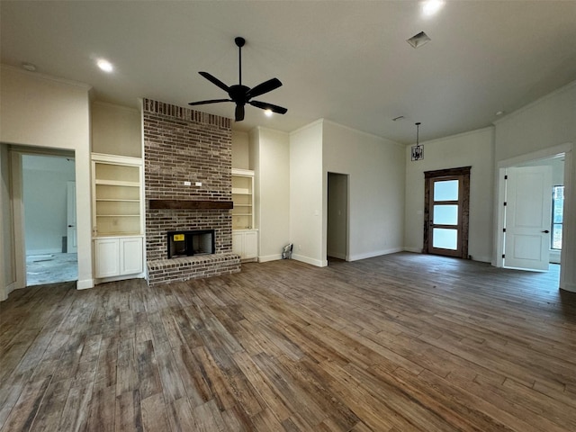 unfurnished living room with a fireplace, ceiling fan, built in shelves, and dark hardwood / wood-style floors