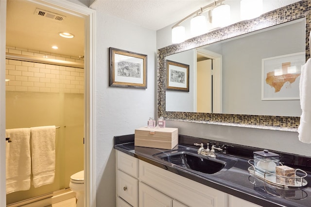 bathroom featuring toilet, vanity, a textured ceiling, and walk in shower