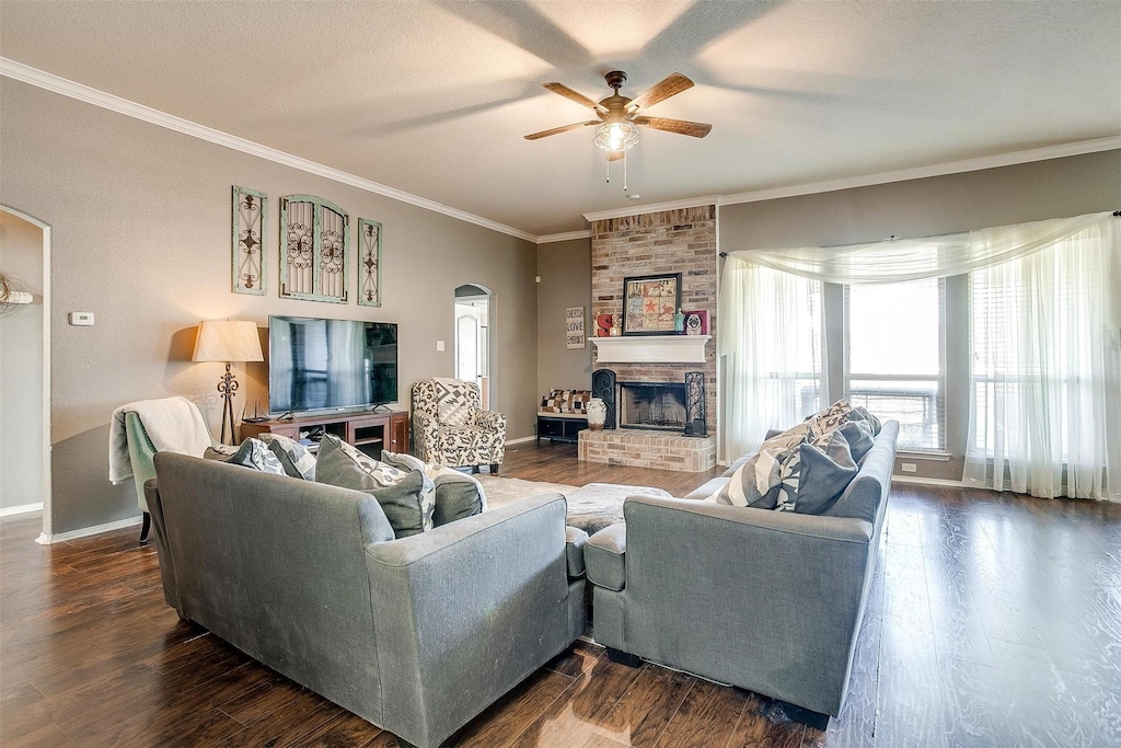 living room with ornamental molding, arched walkways, a brick fireplace, and dark wood finished floors