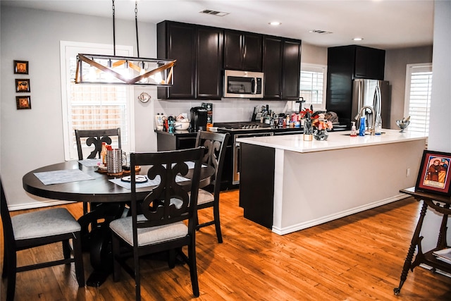 kitchen featuring stainless steel appliances, light wood-type flooring, decorative light fixtures, decorative backsplash, and a kitchen island with sink