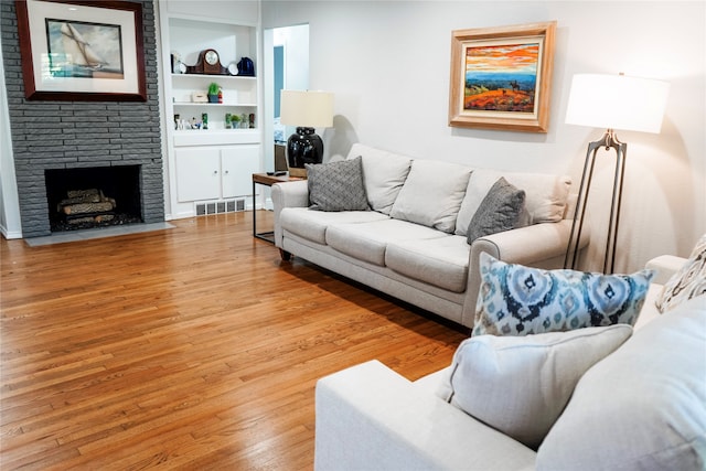 living room with built in features, light wood-type flooring, and a fireplace