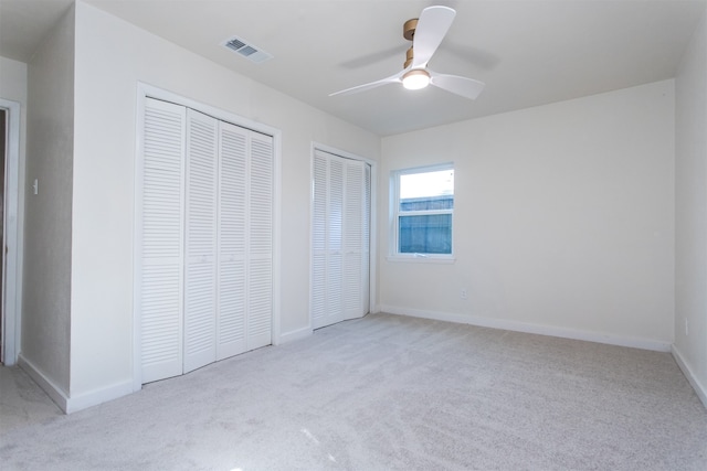 unfurnished bedroom featuring ceiling fan, light carpet, and two closets