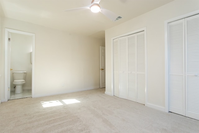 unfurnished bedroom featuring multiple closets, light colored carpet, ceiling fan, and ensuite bath