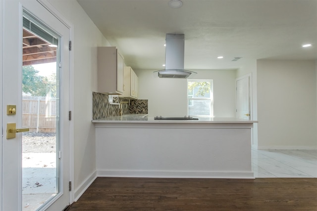 kitchen with island range hood, tasteful backsplash, white cabinetry, and plenty of natural light