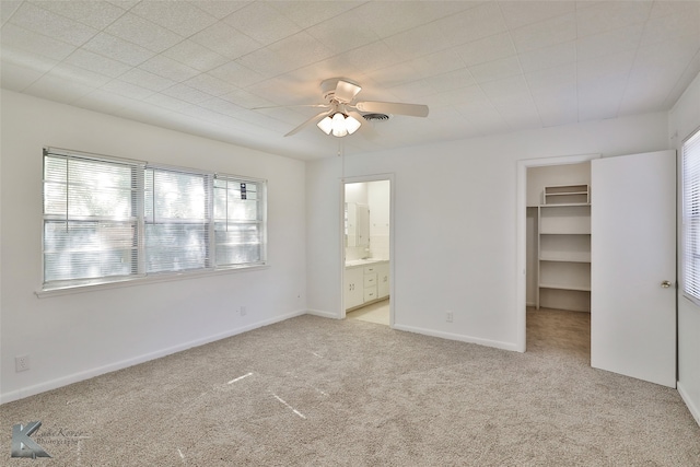 unfurnished bedroom featuring light carpet, connected bathroom, ceiling fan, a closet, and a spacious closet