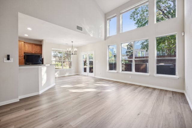 unfurnished living room featuring french doors, a towering ceiling, light hardwood / wood-style floors, and a notable chandelier