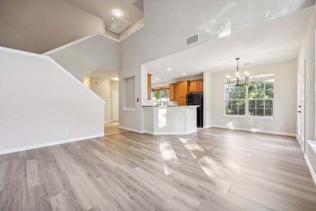 unfurnished living room with a towering ceiling, an inviting chandelier, and light hardwood / wood-style floors