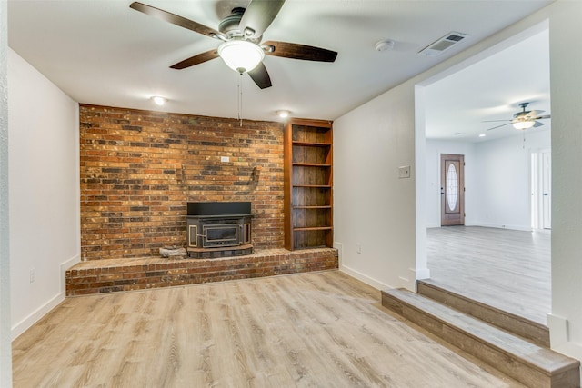 unfurnished living room featuring ceiling fan, a wood stove, built in features, and light hardwood / wood-style floors