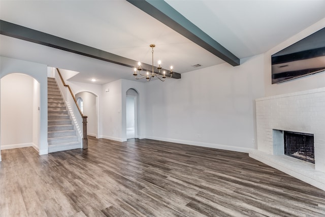 unfurnished living room featuring beamed ceiling, a chandelier, hardwood / wood-style flooring, and a brick fireplace