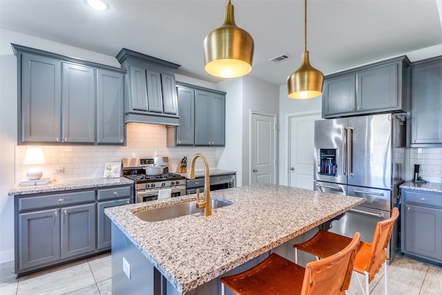 kitchen with decorative backsplash, appliances with stainless steel finishes, hanging light fixtures, and a center island with sink