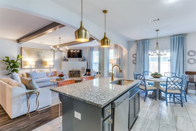 kitchen with a center island with sink, hanging light fixtures, sink, stainless steel dishwasher, and light stone countertops