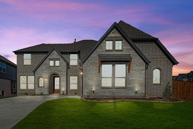 view of front of house with brick siding, fence, concrete driveway, roof with shingles, and a front lawn