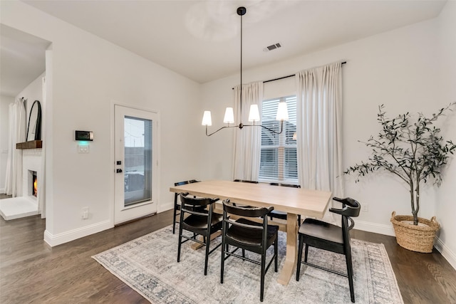 dining room featuring visible vents, baseboards, a chandelier, a lit fireplace, and dark wood-style flooring