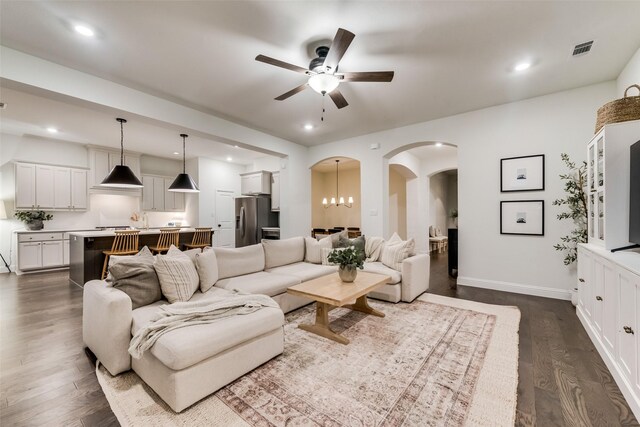 living room with ceiling fan with notable chandelier and dark hardwood / wood-style floors