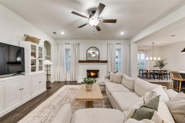 living room with visible vents, ceiling fan with notable chandelier, dark wood finished floors, recessed lighting, and a lit fireplace