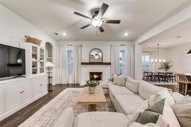 living room featuring ceiling fan with notable chandelier and dark wood-type flooring